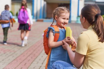 mother accompanies child to school. mom supports and motivates the student.caring mother with tenderness looks at her daughter,passes her book textbook.positive little girl fun going to primary school